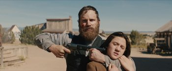 Movie still from “The Kid” (2019), directed by Vincent D'Onofrio – A man and a woman holding a gun in a field; Medium shot, Low angle
