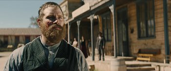 Movie still from “The Kid” (2019), directed by Vincent D'Onofrio – A man with a long beard standing in front of a building; Close Up shot, Low angle