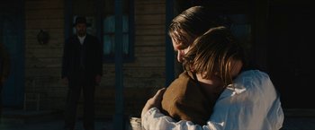 Movie still from “The Kid” (2019), directed by Vincent D'Onofrio – A woman and a boy hug in front of a wooden house; Medium shot, Over the shoulder angle
