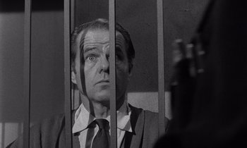 Movie still from “The Killing” (1956), directed by Stanley Kubrick – A man in a suit and tie behind bars; Close Up shot, Low angle