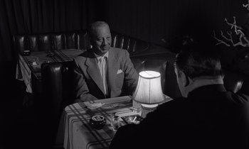 Movie still from “The Killing” (1956), directed by Stanley Kubrick – An older man sitting at a table in a restaurant; Medium shot, Over the shoulder angle