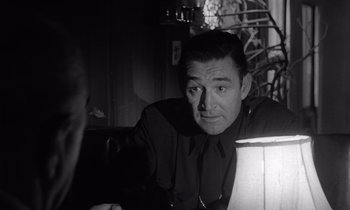 Movie still from “The Killing” (1956), directed by Stanley Kubrick – A black - and - white photo of a man sitting at a table; Close Up shot, Over the shoulder angle