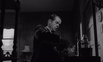 Movie still from “The Killing” (1956), directed by Stanley Kubrick – A black - and - white photo of a man preparing a drink; Medium shot, Low angle