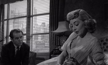 Movie still from “The Killing” (1956), directed by Stanley Kubrick – An old photo of a man and a woman sitting in front of a window; Medium shot, Over the shoulder angle