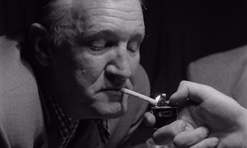 Movie still from “The Killing” (1956), directed by Stanley Kubrick – An older man smoking a cigarette with a lighter in his mouth; Close Up shot, Low angle