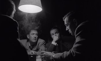 Movie still from “The Killing” (1956), directed by Stanley Kubrick – A group of men sitting at a table in front of a lamp; Medium shot, Over the shoulder angle