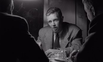 Movie still from “The Killing” (1956), directed by Stanley Kubrick – A black and white photo of a man sitting at a table; Medium shot, Over the shoulder angle