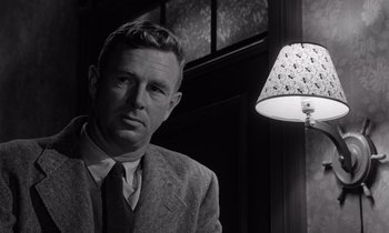 Movie still from “The Killing” (1956), directed by Stanley Kubrick – A black and white photo of a man standing next to a lamp; Close Up shot, Low angle