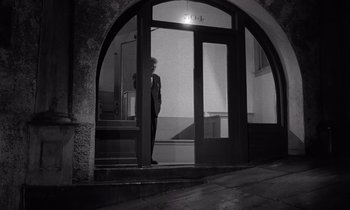 Movie still from “The Killing” (1956), directed by Stanley Kubrick – A man in a suit standing in front of an open door; Wide shot, High angle