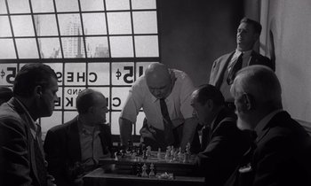 Movie still from “The Killing” (1956), directed by Stanley Kubrick – A group of men playing a game of chess in a room; Medium shot, Over the shoulder angle