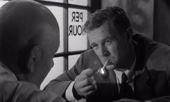 Movie still from “The Killing” (1956), directed by Stanley Kubrick – A black and white photo of a man smoking a cigarette; Close Up shot, Over the shoulder angle