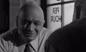 Movie still from “The Killing” (1956), directed by Stanley Kubrick – An older bald man wearing a neck tie; Close Up shot, Over the shoulder angle