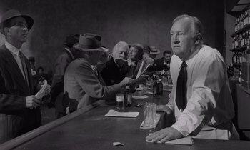Movie still from “The Killing” (1956), directed by Stanley Kubrick – A man sitting at a table with a bunch of other men; Medium shot, Low angle