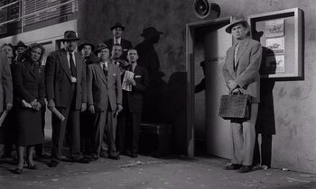 Movie still from “The Killing” (1956), directed by Stanley Kubrick – A black and white photo of a group of men standing in front of an elevator; Wide shot, Low angle