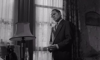 Movie still from “The Killing” (1956), directed by Stanley Kubrick – A black and white photo of a man standing in front of a window; Medium shot, Low angle
