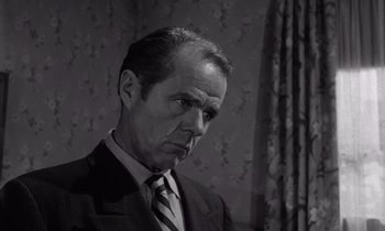 Movie still from “The Killing” (1956), directed by Stanley Kubrick – An older man wearing a suit and tie in front of a wall; Close Up shot, Low angle