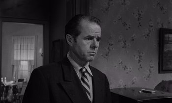 Movie still from “The Killing” (1956), directed by Stanley Kubrick – A man in a suit and tie in front of a wall; Close Up shot, Low angle