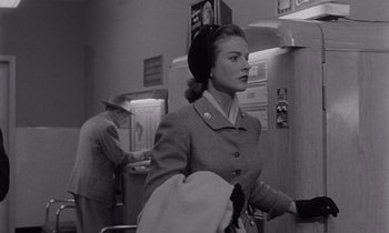 Movie still from “The Killing” (1956), directed by Stanley Kubrick – A woman wearing a hat and a coat walking in a room; Medium shot, Low angle