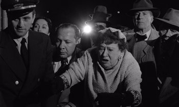 Movie still from “The Killing” (1956), directed by Stanley Kubrick – An older woman is crying in a crowd of onlookers; Medium shot, High angle
