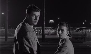 Movie still from “The Killing” (1956), directed by Stanley Kubrick – A man and a woman standing next to each other on the street; Medium shot, Low angle