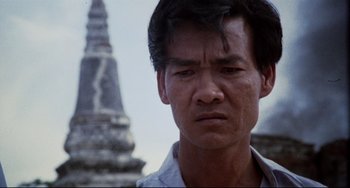 Movie still from “The Killing Fields” (1984), directed by Roland Joffé – A man's face in front of a building; Close Up shot, Low angle