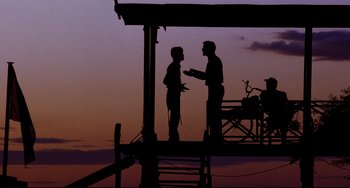 Movie still from “The Killing Fields” (1984), directed by Roland Joffé – Two men standing next to each other in front of a sky background; Wide shot, Low angle