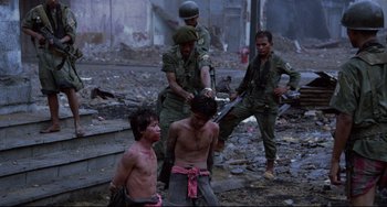 Movie still from “The Killing Fields” (1984), directed by Roland Joffé – A group of men standing next to each other in the rubble; Wide shot, Over the shoulder angle
