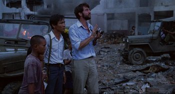 Movie still from “The Killing Fields” (1984), directed by Roland Joffé – A man standing next to a group of people; Medium shot, Over the shoulder angle