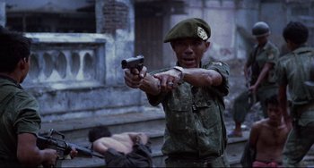 Movie still from “The Killing Fields” (1984), directed by Roland Joffé – A man holding a gun while standing on a street; Medium shot, Low angle