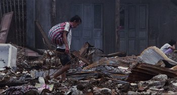 Movie still from “The Killing Fields” (1984), directed by Roland Joffé – A man walking through rubble with a backpack on his back; Wide shot, Over the shoulder angle