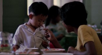 Movie still from “The Killing Fields” (1984), directed by Roland Joffé – A man and a boy are eating at a table; Close Up shot, Over the shoulder angle