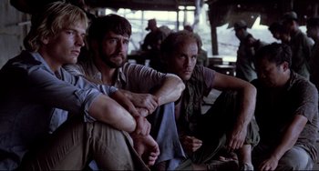 Movie still from “The Killing Fields” (1984), directed by Roland Joffé – A group of men sitting next to each other on the ground; Medium shot, Low angle