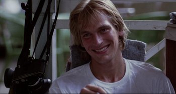 Movie still from “The Killing Fields” (1984), directed by Roland Joffé – A person sitting in a chair smiling; Close Up shot, Low angle
