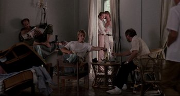 Movie still from “The Killing Fields” (1984), directed by Roland Joffé – A group of people sitting around a living room together; Wide shot, Low angle