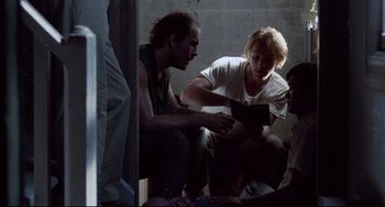Movie still from “The Killing Fields” (1984), directed by Roland Joffé – A group of people sitting around a room; Medium shot, Over the shoulder angle