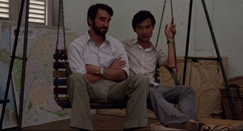 Movie still from “The Killing Fields” (1984), directed by Roland Joffé – A couple of men sitting next to each other on a swing; Medium shot, Low angle
