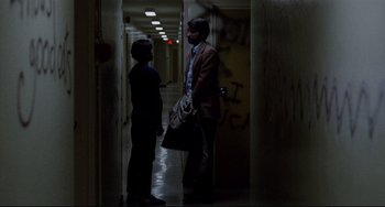 Movie still from “The Killing Fields” (1984), directed by Roland Joffé – A man and a woman standing in a hallway talking; Wide shot, Over the shoulder angle