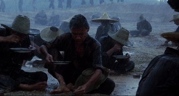 Movie still from “The Killing Fields” (1984), directed by Roland Joffé – A group of people sitting on the ground in the rain; Wide shot, High angle