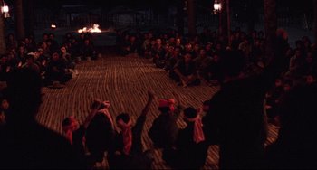 Movie still from “The Killing Fields” (1984), directed by Roland Joffé – A group of people sitting on the ground in front of a crowd; Wide shot, High angle