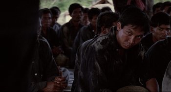 Movie still from “The Killing Fields” (1984), directed by Roland Joffé – A large group of people sitting in a room together; Medium shot, Over the shoulder angle