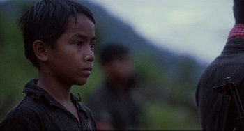 Movie still from “The Killing Fields” (1984), directed by Roland Joffé – A young boy standing in front of a group of people; Close Up shot, Low angle