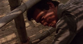 Movie still from “The Killing Fields” (1984), directed by Roland Joffé – A man is leaning against a bamboo pole; Close Up shot, High angle