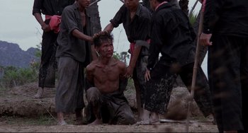 Movie still from “The Killing Fields” (1984), directed by Roland Joffé – A group of men standing around a man with a head shaved; Wide shot, High angle