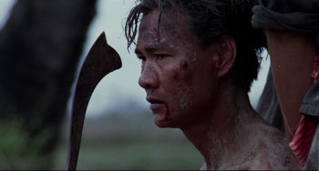 Movie still from “The Killing Fields” (1984), directed by Roland Joffé – A man with a bloody face holding an axe; Close Up shot, Over the shoulder angle