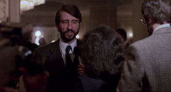 Movie still from “The Killing Fields” (1984), directed by Roland Joffé – A man in a suit is being interviewed by an older woman; Close Up shot, Over the shoulder angle