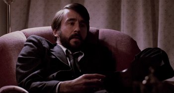 Movie still from “The Killing Fields” (1984), directed by Roland Joffé – A man in a suit and tie sitting in a chair; Close Up shot, Low angle
