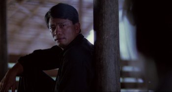 Movie still from “The Killing Fields” (1984), directed by Roland Joffé – A man leaning against a wooden pole in the dark; Medium shot, Low angle