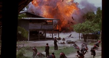 Movie still from “The Killing Fields” (1984), directed by Roland Joffé – A group of people standing in front of an exploding building; Extreme Wide shot, High angle