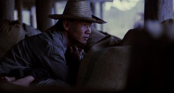 Movie still from “The Killing Fields” (1984), directed by Roland Joffé – A man wearing a straw hat sitting on top of a couch; Close Up shot, High angle