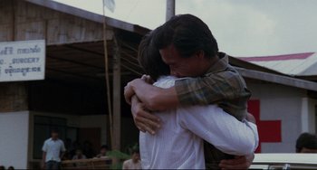 Movie still from “The Killing Fields” (1984), directed by Roland Joffé – Two men hugging each other in front of a building; Medium shot, Over the shoulder angle